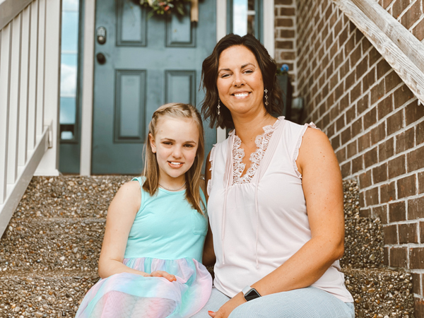 Mother with arm around daughter smiling sitting on front porch