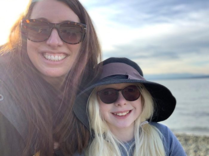 Mother and daughter smiling for camera, both wearing sunglasses, daughter wearing big floppy hat
