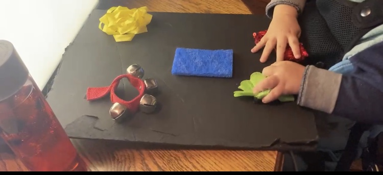 A photo of a toddler's hands exploring several household objects on a tabletop. 