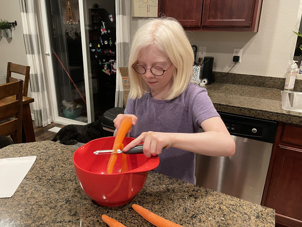 Young girl with glasses peeling a carrot into a bowl.