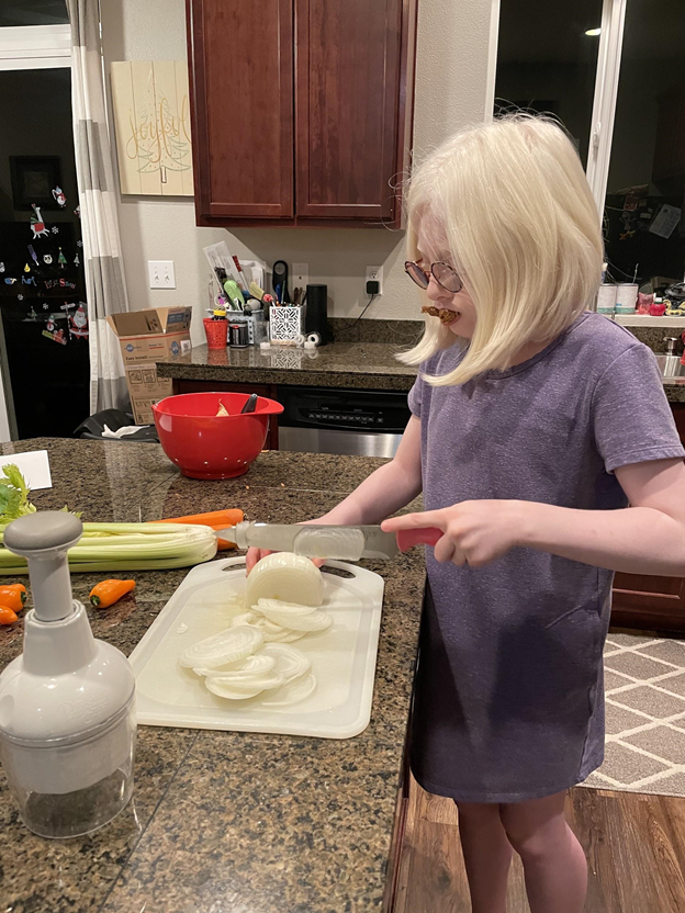 Young girl with glasses chopping an onion.