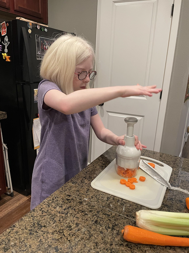 Young girl with glasses using a chopping tool to chop carrots,