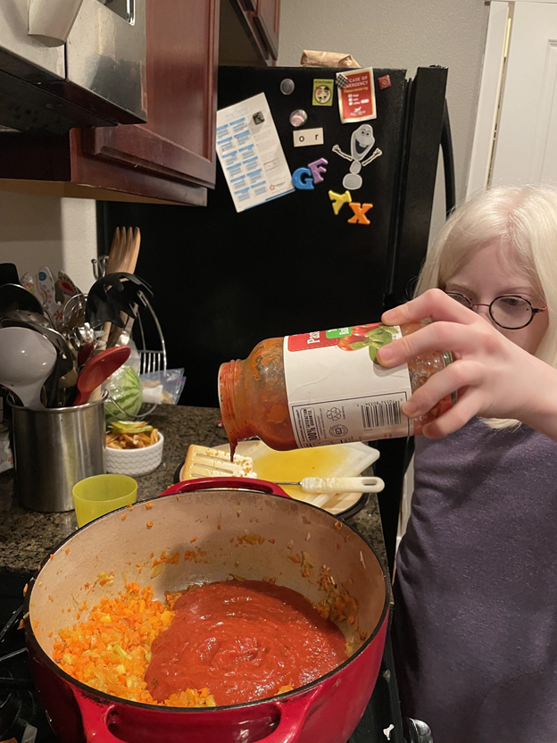Young girl with glasses pouring pasta sauce into a pot.