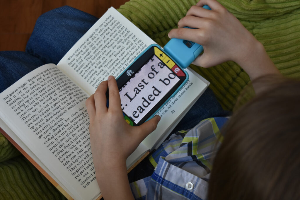 Child using a video magnifier reading a book. 