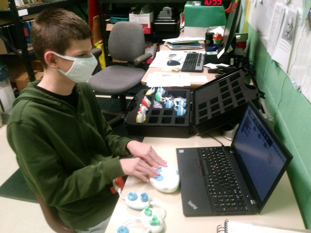 Russell at school using code jumper. He is sitting at a desk in front of his laptop and is manipulating the pieces of code jumper. 