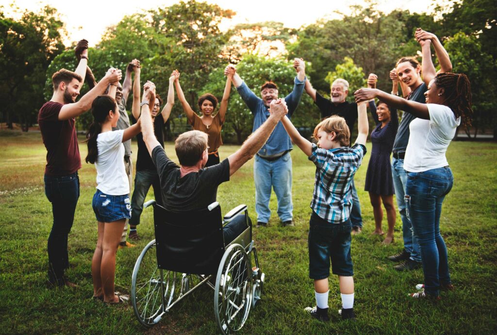 A group of people of all ages standing outside in a circle all holding hands raised in the air. 