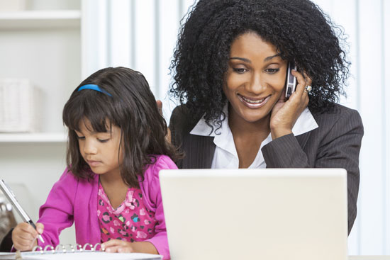 Mother at computer and on cell phone with daughter on her lap. 