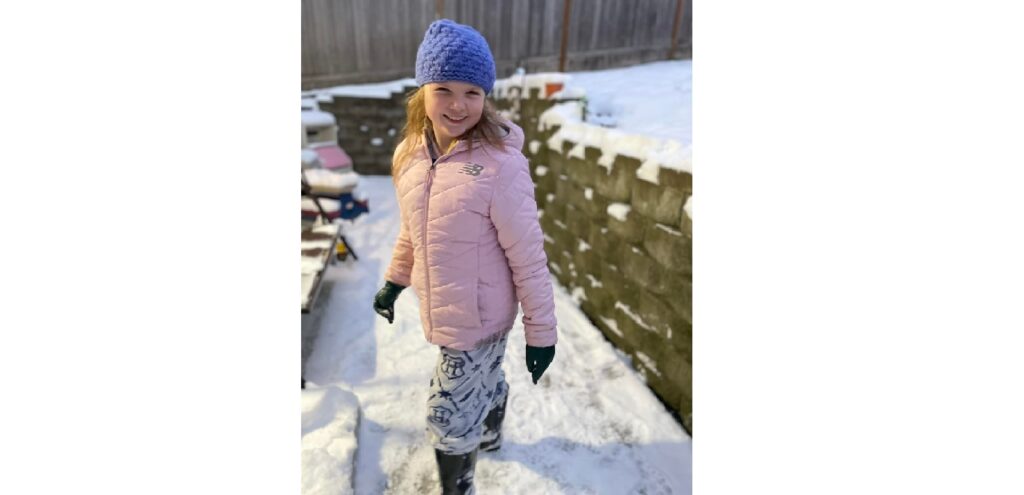 Photo of young girl wearing a winter hat and coat out in the snow. 