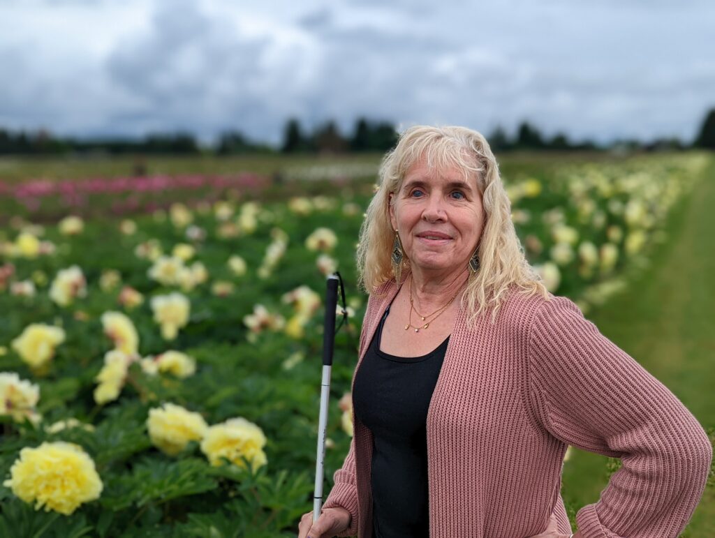 image of Gena holding cane in front of a field of yellow flowers 