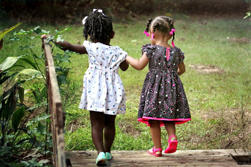 two preschool-age girls crossing a wooden bridge in a park 