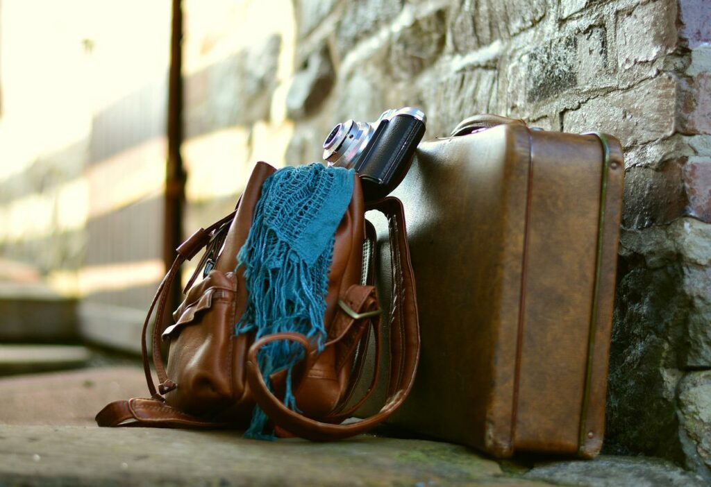 Camera resting on a suitcase and backpack on the ground against a brick wall. 