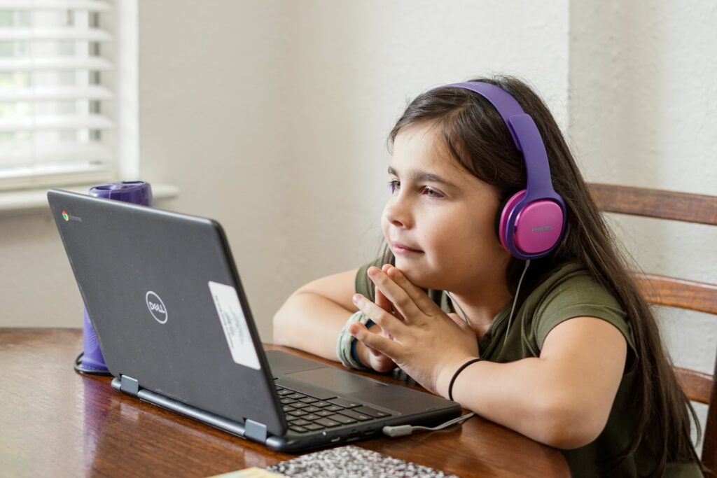 A young sitting at a table wearing headphones and looking at her laptop computer. 
