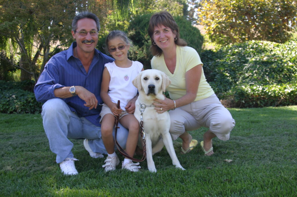 Man, woman, child, and wheat-colored dog pose in the grass.