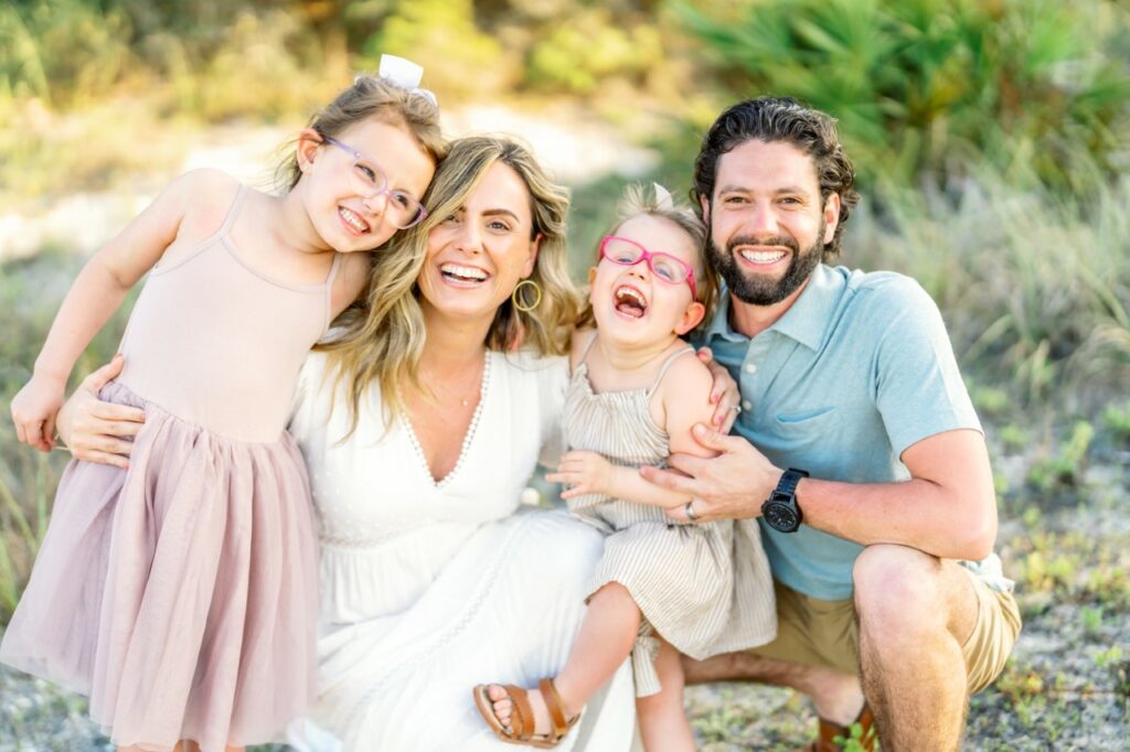 An image of the Spirito family outdoors, Mom and Dad with their arms around two young, smiling girls wearing pink glasses.