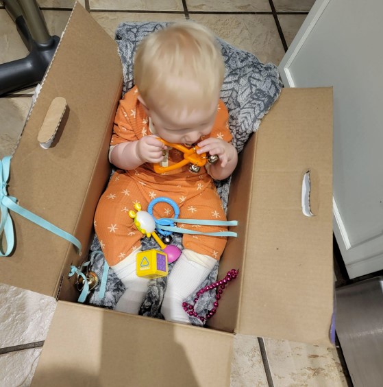 Dominic is sitting in the diaper box and exploring bells.