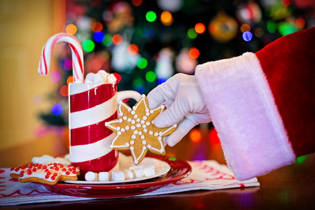 Santa's hand clutching a ginger bread cookie left on a plate alongside a cup of hot cocoa.