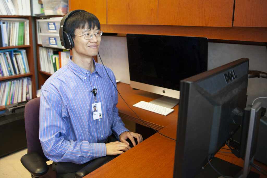 Individual working on a computer while wearing eyeglasses and headphones