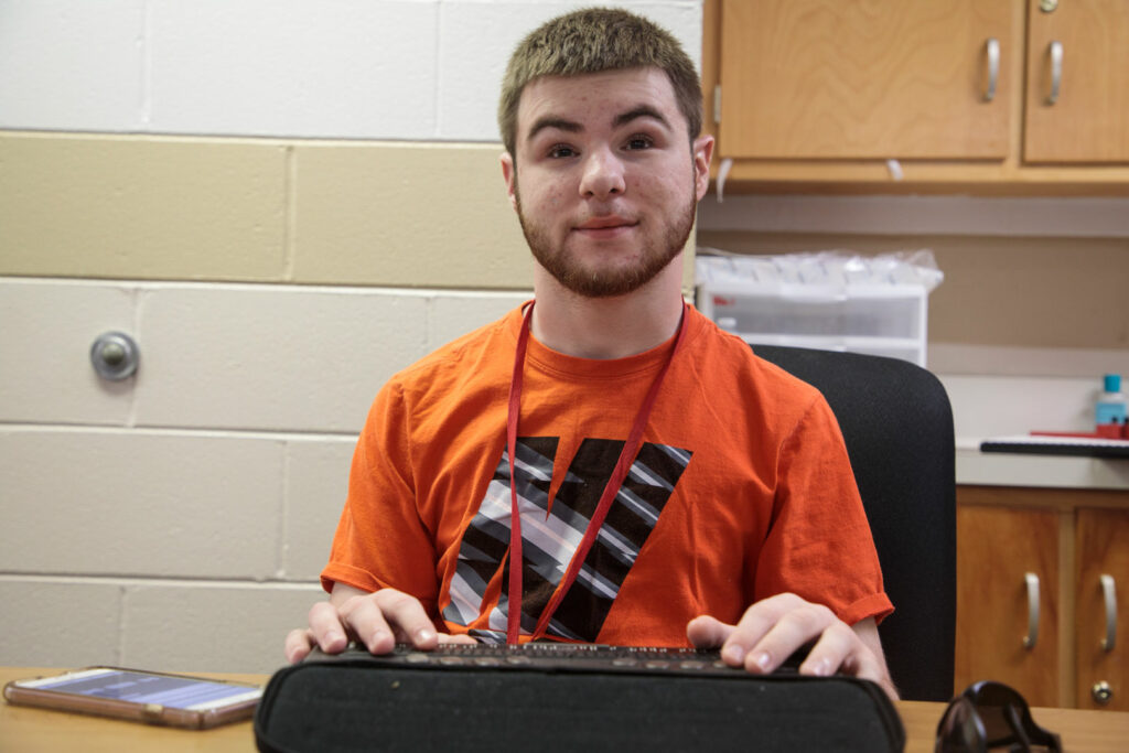 A teenager sitting at a table using a refreshable braille display.