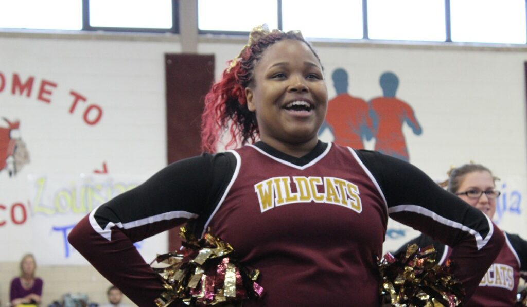 Cheerleader mid-cheer wearing “Wildcats” uniform.