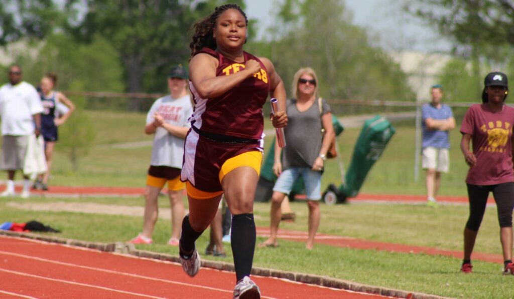 Teen runs on a track and carries a baton