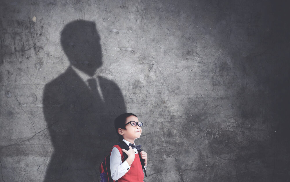 Happy schoolboy standing with his shadow on the wall while imagining be a businessman.